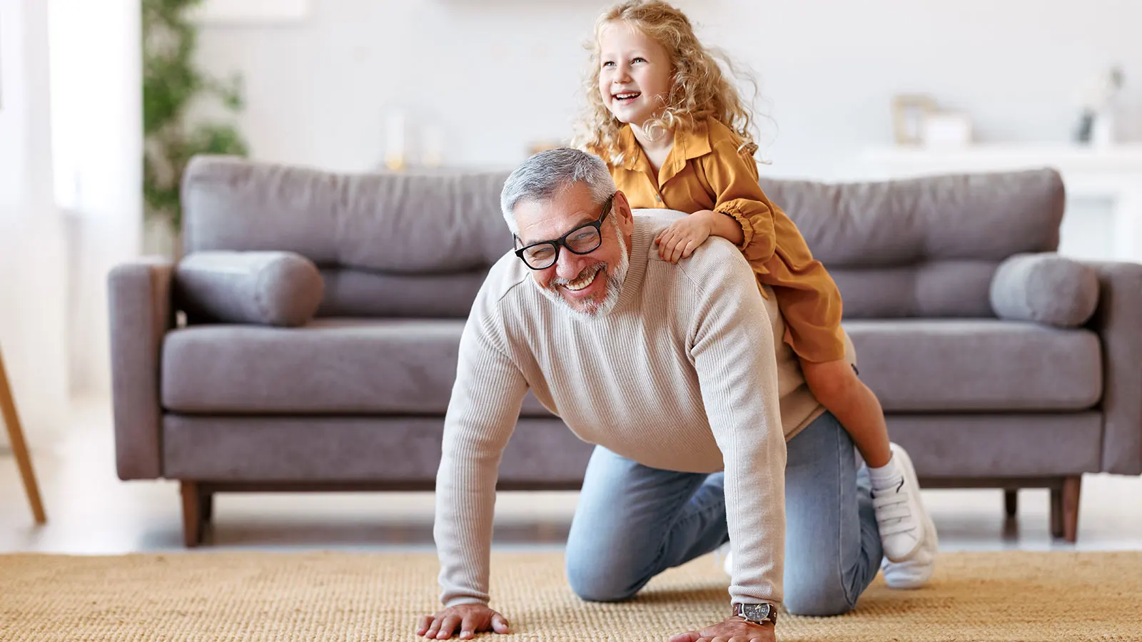 Senior man grandpa giving piggyback to excited child and smiling at camera.